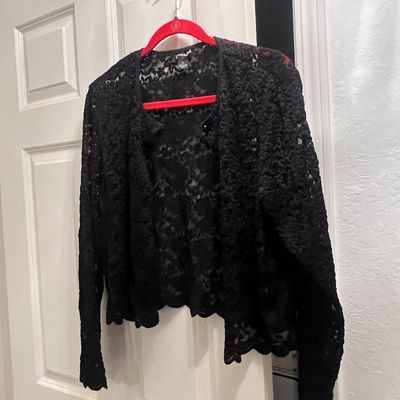Black lace open-front jacket or cardigan, hanging on a red hanger in gently used condition.