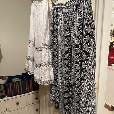 Two bohemian-style skirts hanging on a door, including a white sequin-trimmed tiered skirt and a black-and-white patterned maxi skirt.
