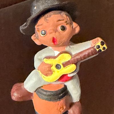 Sale Photo Thumbnail #120: Hand-painted miniature terracotta figurine depicting a boy playing a guitar while seated on a barrel, mid-20th century.