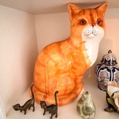 Sale Photo Thumbnail #24: Large ceramic orange tabby cat figurine, displayed alongside two small black metal cat figurines and a stone pear on a shelf.