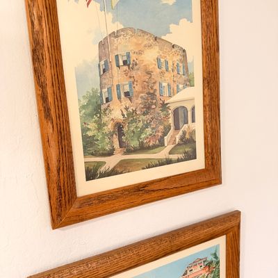Sale Photo Thumbnail #53: Pair of framed watercolor-style prints depicting historic buildings, including the Blackbeard's Castle tower in St. Thomas, housed in matching oak wood frames.