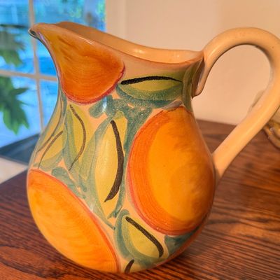 Sale Photo Thumbnail #94: Hand-painted ceramic pitcher featuring a colorful orange citrus motif with green leaves, displayed on a wooden surface.