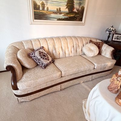 Sale Photo Thumbnail #2: Vintage cream-colored damask sofa featuring a channel-tufted back, curved wooden arm accents, and coordinating throw pillows.