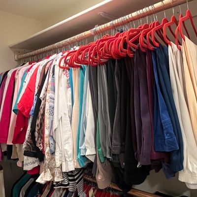 Closet rod filled with women's modern and vintage apparel on red felt velvet hangers, including pants, blouses, and jackets.
