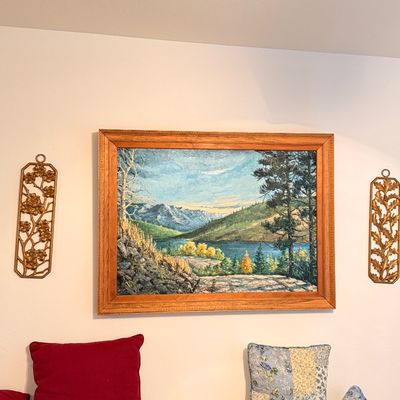 Sale Photo Thumbnail #41: Large framed oil painting depicting a mountain lake landscape, flanked by a pair of vintage gold-tone metal floral wall plaques.