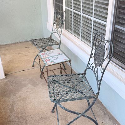 Sale Photo Thumbnail #55: Three-piece wrought iron bistro set featuring two folding chairs with lattice seats and a small side table with a decorative tiled top.