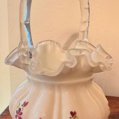 Sale Photo Thumbnail #76: Fenton-style hand-painted milk glass basket featuring a ruffled rim, ribbed body, clear glass handle, and delicate purple floral details.