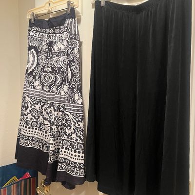 Two long women's skirts, including one with a black-and-white paisley boho print and one solid black skirt, both hanging on a door.