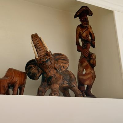 Sale Photo Thumbnail #29: Collection of hand-carved wooden sculptures, including an elephant with raised trunk and a standing human figure, displayed on a shelf.