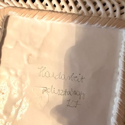 Sale Photo Thumbnail #117: Underside of a white ceramic reticulated woven basket, featuring hand-written inscriptions including "Handarbeit" and "dísztárgy".