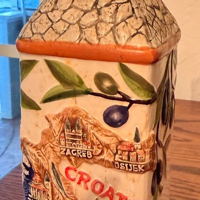 Sale Photo Thumbnail #68: Vintage souvenir ceramic decanter from Croatia featuring embossed illustrations of major cities, an olive branch motif, and a cobblestone-textured neck.