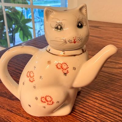 Sale Photo Thumbnail #80: Vintage white porcelain cat teapot featuring hand-painted floral details, gold collar accents, and a raised paw spout.