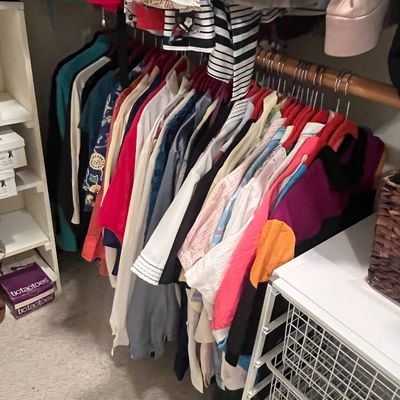 Closet rod filled with various women's shirts, blouses, and tops on velvet hangers.