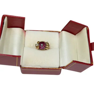 Sale Photo Thumbnail #66: Vintage gold ring featuring a central red stone accented with small diamonds, presented in a red leatherette double-door presentation box.