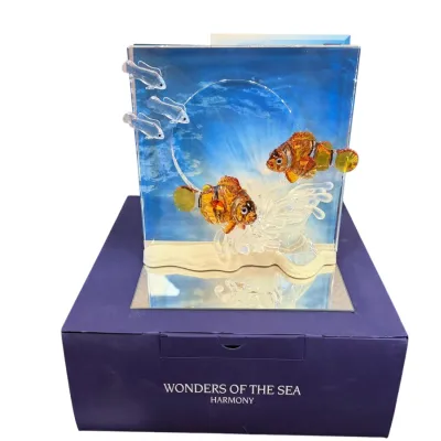 Sale Photo Thumbnail #23: Swarovski crystal "Wonders of the Sea - Harmony" clownfish figurine, featuring two orange clownfish and three small clear fish against a blue ocean backdrop, displayed on its original blue box.
