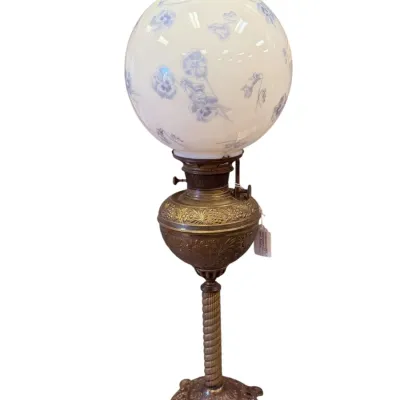 Sale Photo Thumbnail #22: Antique banquet lamp featuring an ornate brass base with a spiral column and a white milk glass globe shade decorated with blue floral motifs.