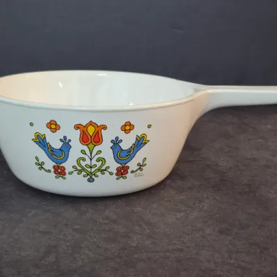 Vintage Corning Ware 'Country Festival' pattern saucepan with handle, featuring a colorful folk art design of bluebirds and a...