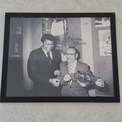 Framed black and white photograph featuring Muhammad Ali and Carmen Basilio, signed by Carmen Basilio in black ink.