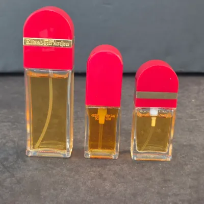 Three vintage Elizabeth Arden Red Door perfume bottles in varying sizes, featuring their signature red caps and gold-tone accents.
