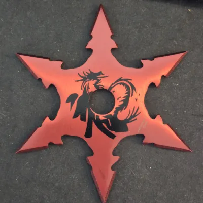 Six-pointed red metallic throwing star featuring a black dragon graphic around the center hole.