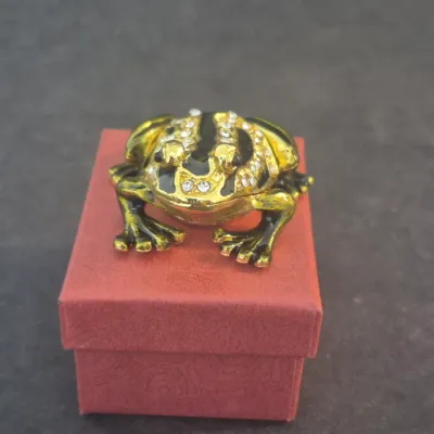 Jeweled frog trinket box with gold-tone and black enamel finish, accented with rhinestones, sitting atop a small red gift box.