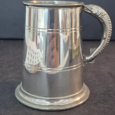 Vintage Sheffield pewter tankard featuring a polished finish, incised horizontal bands, and a detailed fish-shaped handle.