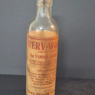 Antique Nerv-Worth patent medicine bottle from Zanesville, Ohio, featuring its original paper label with aged wear and staining.