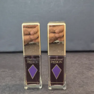Two vintage bottles of Elizabeth Taylor's Passion perfume, featuring gold-toned caps and purple diamond labels.