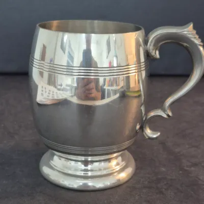 Vintage Tudric pewter tankard featuring a polished finish, horizontal incised lines, and an ornate scroll handle.