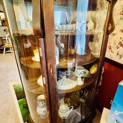 Sale Photo Thumbnail #25: Antique bowfront wood curio cabinet with curved glass panels, claw feet, and multiple shelves displaying glassware and ceramics.