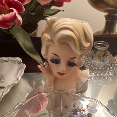 Sale Photo Thumbnail #69: Vintage mid-century ceramic lady head vase featuring blonde hair, long eyelashes, and a pearl earring, displayed alongside floral glassware.