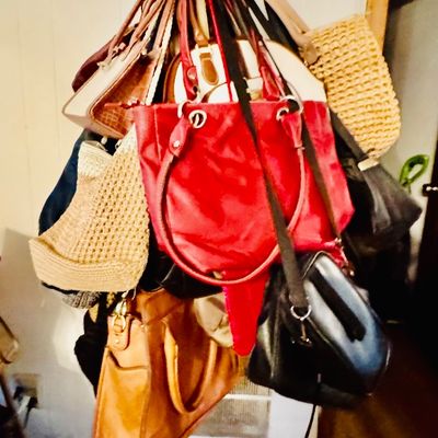 Sale Photo Thumbnail #11: A collection of assorted women's handbags, including leather, woven straw, and fabric styles, displayed on a brass coat rack.