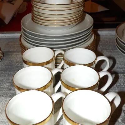 Sale Photo Thumbnail #51:  Fine china featuring white ribbed porcelain with elegant gold trim, including a stack of plates, saucers, and matching coffee mugs.