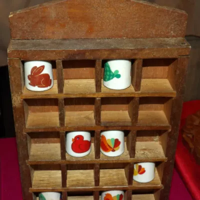 Sale Photo Thumbnail #16: Vintage wooden thimble display case containing seven porcelain thimbles decorated with colorful animal motifs, including a rabbit, duck, and turkey.