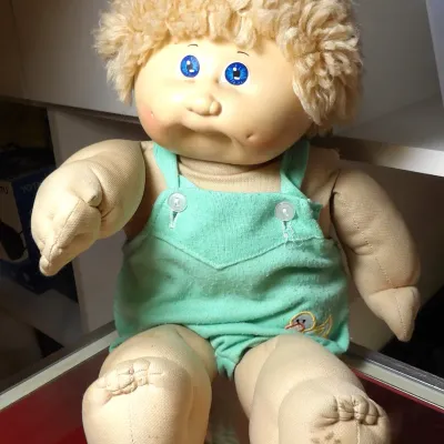 Sale Photo Thumbnail #6: Vintage Coleco Cabbage Patch Kids doll featuring blonde yarn hair, blue eyes, and a green romper with a duck motif, showing some wear and minor staining on the feet.
