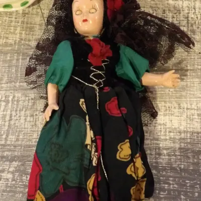 Sale Photo Thumbnail #48: Vintage hard plastic souvenir doll dressed in a traditional Spanish costume, featuring a black lace mantilla, red hair rose, and a colorful floral skirt.