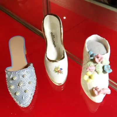 Sale Photo Thumbnail #26: Trio of vintage miniature collectible shoes, including a blue beaded mule, a white porcelain pump with gold trim marked 'allures', and a white porcelain shoe adorned with pastel floral details.