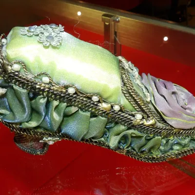 Sale Photo Thumbnail #31: Ornate Victorian-style decorative shoe pin cushion, featuring green and purple satin fabric, metallic trim, faux pearls, and floral embellishments.