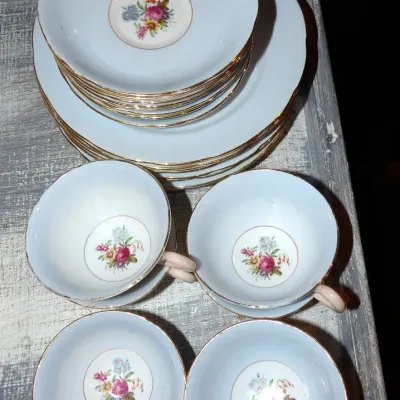 Sale Photo Thumbnail #42: Vintage porcelain tea set featuring four teacups, saucers, and plates, decorated with a central floral motif, light blue glaze, and gold-gilded rims.