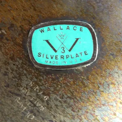 Sale Photo Thumbnail #19: Wallace Silverplate maker's mark and label on a tarnished silver-plated piece, showing the brand's signature teal sticker and engraved markings.