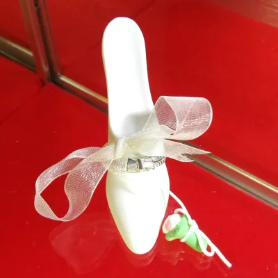 Sale Photo Thumbnail #27: Vintage white porcelain high heel shoe figurine, adorned with a sheer white ribbon, a silver-tone buckle detail, and a small clay rosebud accent.
