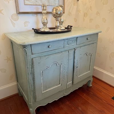 French Country style light green painted sideboard cabinet featuring distressed finish, raised panel doors, and two top drawers.