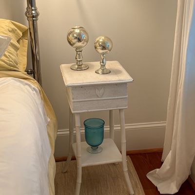 White painted faux bamboo nightstand featuring a woven drawer face and a lower shelf with decorative items.
