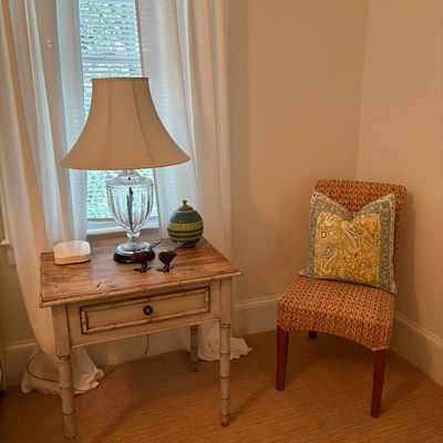 Faux bamboo end table with a distressed off-white base and wood plank top, paired with a woven wicker side chair featuring a paisley...