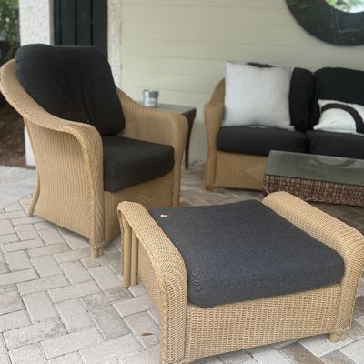 Outdoor wicker patio seating set including a lounge chair, matching ottoman, sofa, and coffee table with dark cushions.
