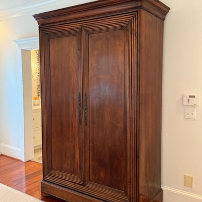 Large French provincial style wooden armoire featuring molded trim detail and ornate brass door handles.