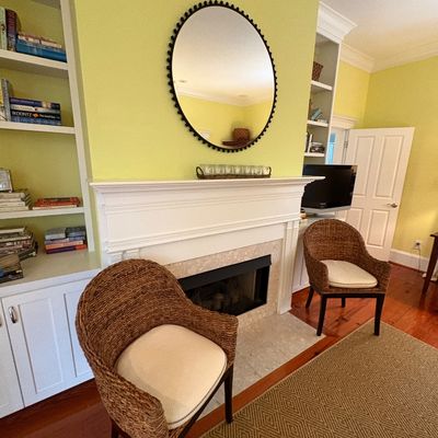 Pair of woven seagrass barrel armchairs with upholstered cushions, flanking a white traditional fireplace mantel.