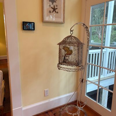 Vintage wrought iron birdcage hanging on a matching scrollwork floor stand, accompanied by framed starfish wall art.