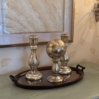Set of three mercury glass decor pieces, including two candle holders and a spherical finial ornament, displayed on an oval wooden tray.