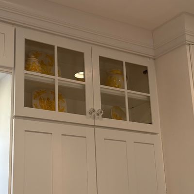 Collection of yellow and white patterned ceramic dinnerware displayed inside glass-front upper kitchen cabinets with clear glass knobs.